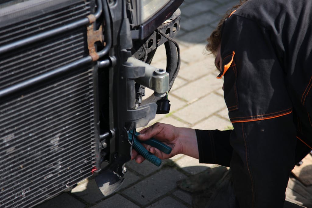 Mechanic working on car repair outdoors using tools, focusing on vehicle radiator area.